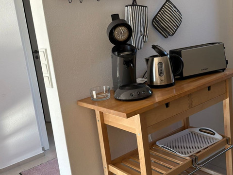 Küche_02 Küchenzeile mit Kaffeemaschine, Toaster und Kochbüchern auf einem Holzregal an einer weißen Wand.