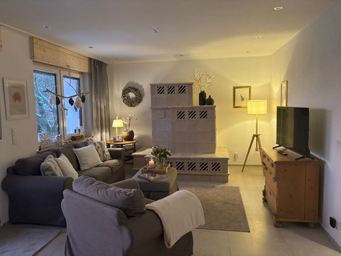 Wohnzimmer Gemütliches Wohnzimmer mit Kachelofen, zwei Sofas, Holzmöbeln und sanfter Beleuchtung.
