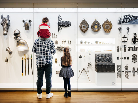 GRASSI Museum für Angewandte Kunst - Museumsbesuch mit der Familie Ein Mann und seine beiden Kinder stehen vor einer Glasvitrine mit verzierten Rüstungsteilen und Metallobjekten im GRASSI Museum für Angewandte KunstA man and his two children stand in front of a glass display case with decorated pieces of armor and metal objects in the GRASSI Museum of Applied ArtsMuž a jeho dvě děti stojí před vitrínou se zdobenými kusy zbroje a kovovými předměty v Muzeu užitého umění GRASSI.Mężczyzna i jego dwoje dzieci stoją przed szklaną gablotą ze zdobionymi elementami zbroi i metalowymi przedmiotami w Muzeum Sztuki Użytkowej GRASSI.Een man en zijn twee kinderen staan voor een glazen vitrine met versierde harnassen en metalen voorwerpen in het GRASSI Museum voor Toegepaste KunstUn uomo e i suoi due figli si trovano davanti a una vetrina con armature decorate e oggetti in metallo nel Museo di Arti Applicate GRASSI