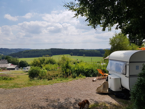 Ausblick vom Campingpark Weiße Wohnwagen auf einem sonnigen Campingplatz mit grünen Feldern und bewaldeten Hügeln im Hintergrund.