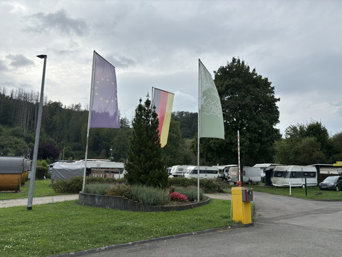 Campingplatz Wiehltal Camper und Fahnen wehen im Wind auf einem Campingplatz, umgeben von bewaldeten Hügeln bei bedecktem Himmel.