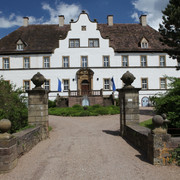 Außenansicht Schloss Wehrden Historisches Schlossgebäude mit weißer Fassade und prächtigem Eingang, umgeben von grünem Garten.