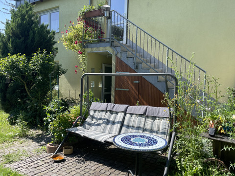 Schaukel im Garten Gemütliche Gartenschaukel auf gepflasterter Terrasse, umgeben von Pflanzen und einem Treppenaufgang.