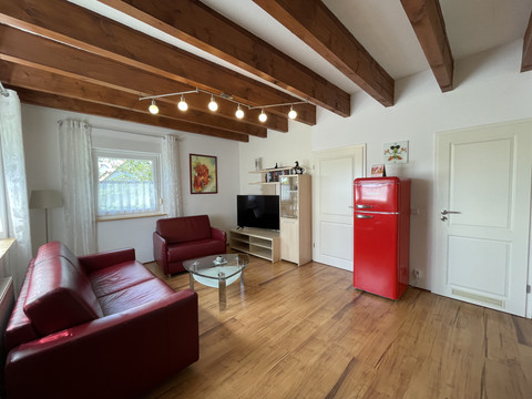 Fewo rot Wohnzimmer im Landhausstil mit Holzbalken, Ledersofas, rotem Retro-Kühlschrank und TV-Schrank.