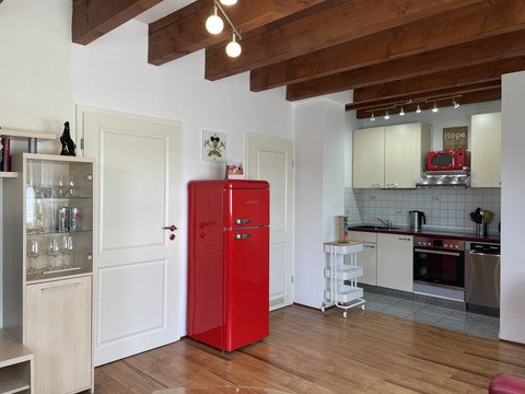 Fewo rot Offene Küche mit weißer Einrichtung, rotem Retro-Kühlschrank und Holzdeckenbalken in modernem Stil.