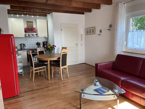 Fewo rot Gemütlicher Wohnbereich mit roten Sofa, Glastisch, Holzboden und Einbauküche in ländlicher Atmosphäre.