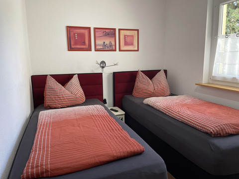 Fewo rot Gemütliches Doppelzimmer mit zwei Einzelbetten, roten Kissenbezügen und Bildern an der Wand.