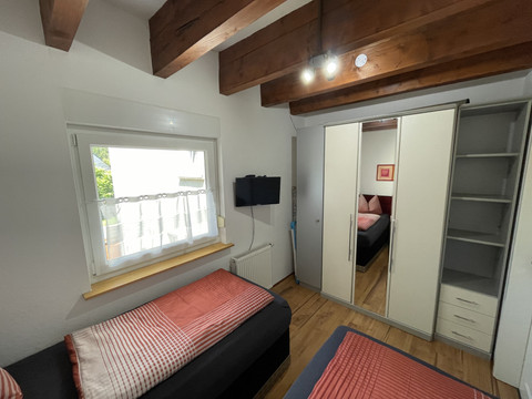 Fewo rot Gemütliches Schlafzimmer mit Holzbalkendecke, zwei Einzelbetten, Kleiderschrank und TV an der Wand.