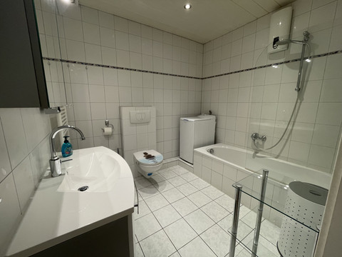 Fewo rot Modernes Badezimmer mit weiß gefliesten Wänden, Badewanne, Waschmaschine und Wand-WC.