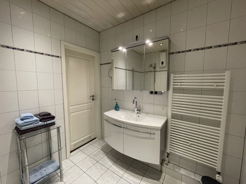 Fewo rot Modernes Badezimmer mit weißen Fliesen, einem Waschbecken unter großem Spiegel und Handtuchhalter.