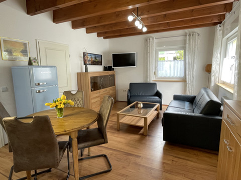 Fewo blau Gemütliches Wohnzimmer mit Holzboden, Ledersofas, Essbereich und helle Fenster mit Vorhängen.