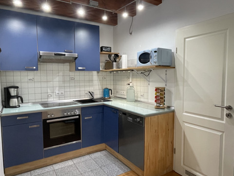 Fewo blau Moderne Küche mit blauen Schränken, Elektroherd, Mikrowelle und Kaffeemaschine, hell erleuchtet.