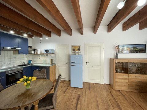 Fewo blau Küche mit Holzbalkendecke, Retro-Kühlschrank, blauem Holz, Esstisch und Sideboard, Blumenstrauß.