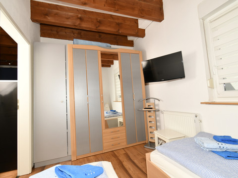 Fewo blau Kleines Schlafzimmer mit Holzbalkendecke, Einzelbett, Schrank, Fernseher an der Wand, und Fenster.