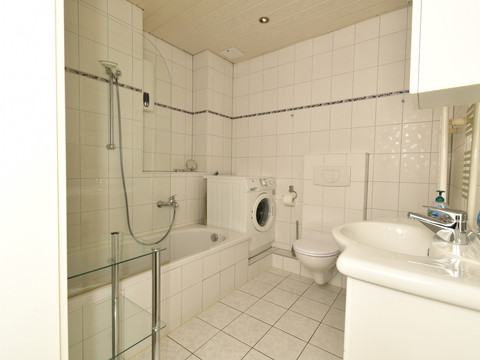 Fewo blau Helles Badezimmer mit Badewanne, Waschmaschine und WC, Fliesen in Weiß, ansprechend und modern.