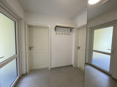 Flur Fewo grün Leerer, heller Flur mit zwei weißen Türen, großen Fenstern links und rechts und einer Garderobe an der Wand.