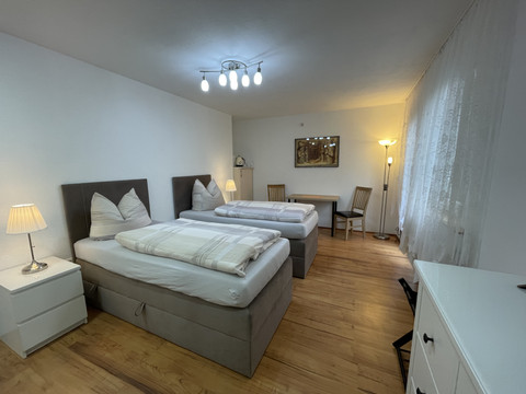 Schlafzimmer Fewo grün Geräumiges Zimmer mit zwei Einzelbetten, Holzboden, Schreibtisch und warmem Lampenlicht.