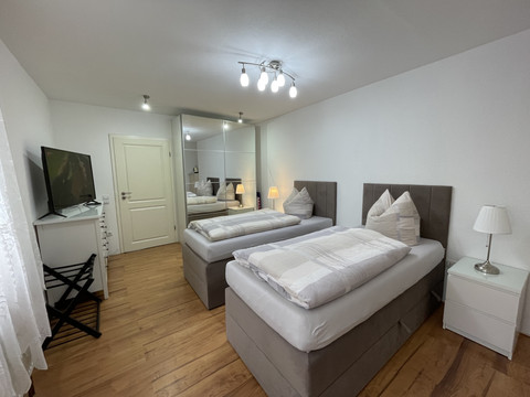 Schlafzimmer Fewo grün Helles Gästezimmer mit zwei Einzelbetten, Holzboden, weißer Einrichtung und stilvoller Beleuchtung.
