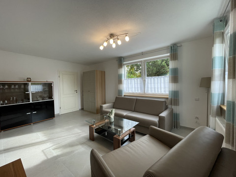 Wohnzimmer Fewo grün Wohnzimmer mit modernen Möbeln, zwei Sofas, Sessel, Glastisch und großer Fensterfront.
