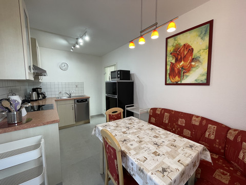 Küche Fewo grün Kleine, moderne Küche mit Esstisch, rotem Sofa, Kunstbild an der Wand und heller Beleuchtung.