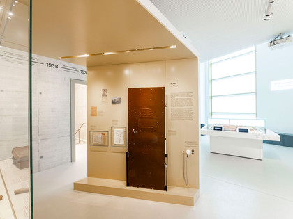 Gedenkstätte-JVA-WF-Ausstellung-Tür.jpg Heller Ausstellungsraum, im Zentrum eine braune ZellentürBright exhibition room, a brown cell door in the centerLyst udstillingsrum, en brun celledør i midtenLichte tentoonstellingsruimte, een bruine celdeur in het midden