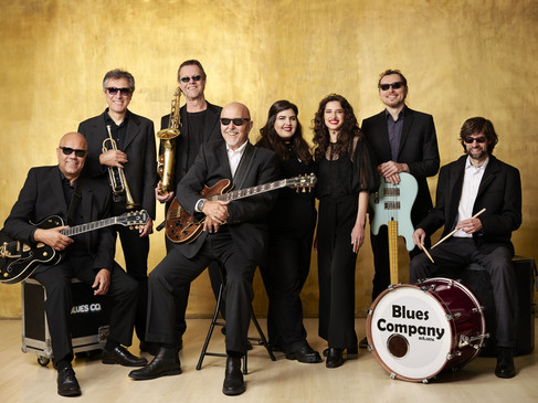 Eine Bluesband mit acht Mitgliedern, alle in schwarzer Kleidung. Musiker mit Gitarren, Saxophon und Schlagzeug.