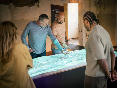 Schloss Colditz - Sehenswürdigkeiten in der Leipzig Region Mehrere Personen betrachten im Schloss Colditz das Relief des Tiergartens auf einer beleuchteten Karte und tauschen sich darüber aus, Schlösserland Sachsen, AusflugSeveral people look at the relief of the zoo on an illuminated map in Colditz Castle and discuss it, Schlösserland Sachsen, ExcursionNěkolik lidí si prohlíží reliéf zoologické zahrady na osvětlené mapě na zámku Colditz a diskutuje o něm, Schlösserland Sachsen, ExcursionKilka osób przygląda się płaskorzeźbie zoo na podświetlanej mapie w zamku Colditz i dyskutuje na jej temat, Schlösserland Sachsen, WycieczkaVerschillende mensen kijken naar het reliëf van de dierentuin op een verlichte kaart in kasteel Colditz en discussiëren erover, Schlösserland Sachsen, ExcursieDiverse persone guardano il rilievo dello zoo su una mappa illuminata nel castello di Colditz e ne discutono, Schlösserland Sachsen, Escursione