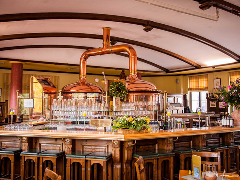 Brausaal Brauhaus "Zum Gießer" Gemütliche Bar mit Holzmöbeln und Kupferbraukesseln, dekoriert mit Blumenarrangements; warme, einladende Atmosphäre.