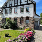 fewo_hermanns_aussenansicht.jpg Zweistöckiges Fachwerkhaus mit Steinbasis, blühenden Beeten und gepflegter Rasenfläche im Vordergrund.