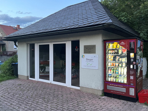 Feuerwehrmuseum Papstdorf mit Proviantomat Kleines Gebäude mit Schieferdach, daneben ein roter Automat mit beleuchteten Flaschen und Snacks.
