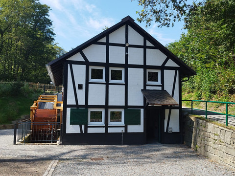 Dümmlinghauser Mühle Fachwerkhaus mit Satteldach in ländlicher Umgebung, umgeben von Bäumen und einem Steinweg.