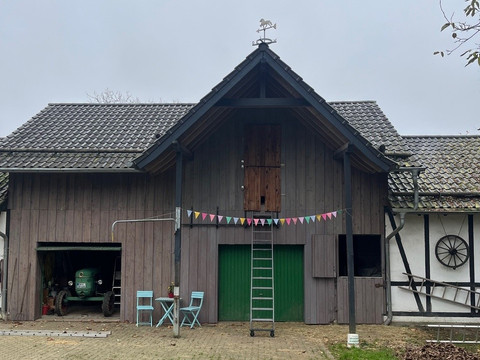 Seelentierzeit Fachwerkhaus mit Scheune, Leiter lehnt an grünen Toren, bunte Wimpelkette und rustikaler Charme.