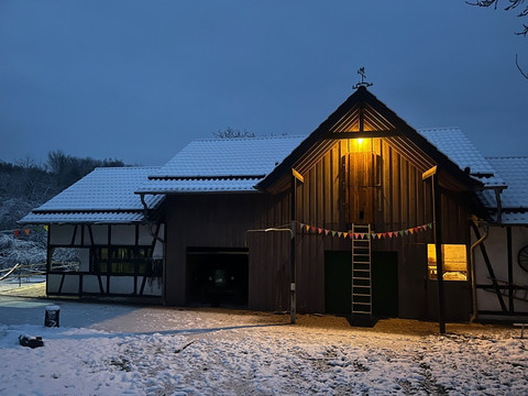 Hof Ein verschneiter Fachwerkhof im Abendlicht, mit festlicher Beleuchtung und sanft beleuchtetem Himmel.