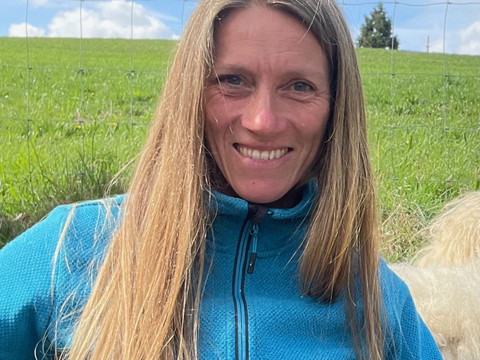 Miriam Mertens Eine Frau mit langen blonden Haaren und blauem Pullover lächelt vor einer grünen Wiese in die Kamera.