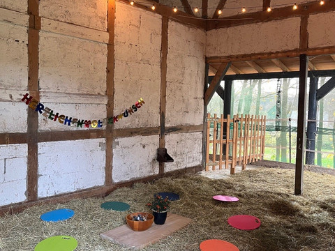 Stall Blick in eine Scheune mit bunten Sitzkissen auf Stroh. Eine Girlande bringt eine festliche Note.