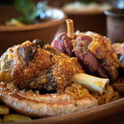 Haxenhaus Knusprige Schweinshaxe und Bratwurst auf einem rustikalen Holzteller mit Sauerkraut serviert.A rustic platter with a crispy pork knuckle, sausages, potatoes, and cabbage on a wooden table.