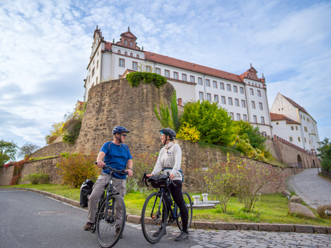 Zwei Radfahrer mit Helm machen einen Stopp vor den Mauern des Schloss Colditz, Schlösserland Sachsen, Aktiv, Ausflug