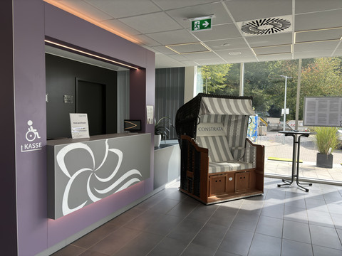 Blütenbad Leichlingen <p>Empfangsbereich mit modernem Tresen, einem Strandkorb und Barhockern in einem lichtdurchfluteten Raum.</p>