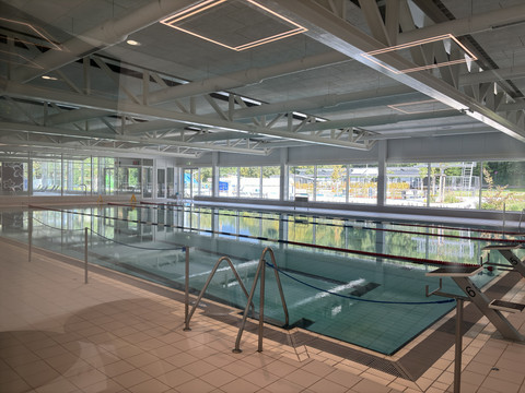 Blütenbad Leichlingen Schwimmbad-Interieur mit hellem Becken, Glaswänden und metallischen Deckenbalken.