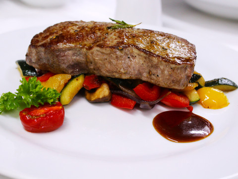 Eimermacher 10.jpg Ein saftiges Steak auf gegrilltem Gemüse, kunstvoll angerichtet mit einem Klecks würziger Sauce auf weißem Teller.