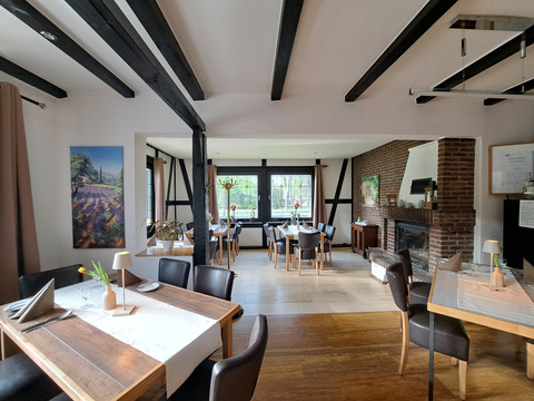 Eimermacher 17.jpg Gemütlicher Gastraum mit Holzbalken, modernem Kamin, gedeckten Tischen und großem Fenster zur Natur.