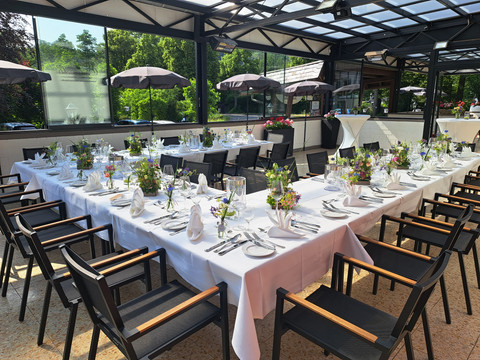 Eimermacher 20.jpg Elegant gedeckte Tafel unter freiem Himmel, umgeben von grüner Natur und dekorativen Blumenarrangements.