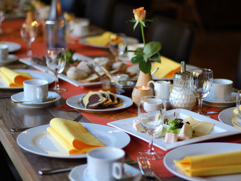 Eimermacher 22.JPG Festlich gedeckter Tisch mit weißen Tellern, gelben Servietten, Gläsern und einer einzelnen Rosenblume.