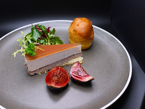 Eimermacher 31.JPG Eine leicht rosa Terrine mit Gelee, dekoriert mit Salat, frischen Feigen und Brötchen auf grauem Teller.