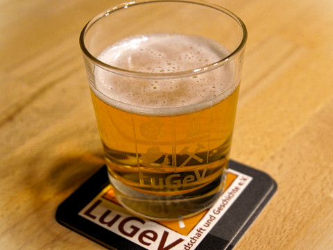 Klosterbier Ein kühles, goldenes Bier in einem Glas auf einem Untersetzer mit "LuGeV" Logo, auf einem Holztisch.