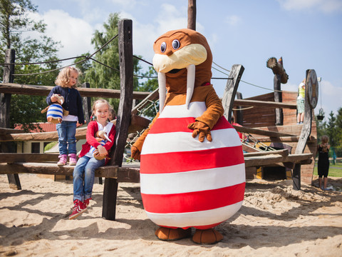 Spielplatz Kinderspielplatz mit Holzstrukturen, fröhlichen Kindern und Maskottchen im gestreiften Kostüm.