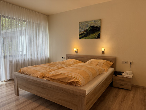 Innenansicht Doppelzimmer Haus Koppelberg Gemütliches Doppelbett in einem hellen Zimmer mit Holzboden und Wandkunst, Tageslicht flutet herein.