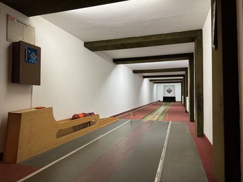 Kegelbahn Haus Koppelberg Eine Kegelbahn mit mehreren Bahnen, bunten Kugeln auf der linken Seite und Holzbalken an der Decke.