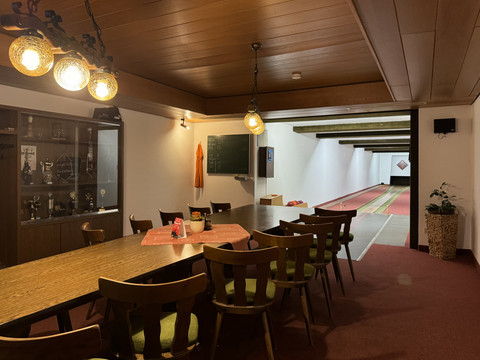 Kegelbahn Haus Koppelberg Gemütlicher Kegelraum mit Holztisch, grünen Stühlen und dekorativen Lampen, beleuchtete Kegelbahn im Hintergrund.