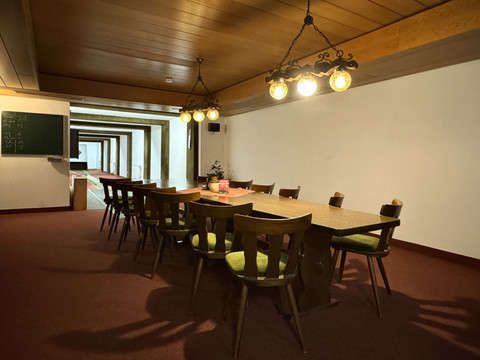 Kegelbahn Haus Koppelberg Langer Tisch mit Holzstühlen in einem Raum mit Holzdecke und vintage Deckenlampen, gemütliche Atmosphäre.